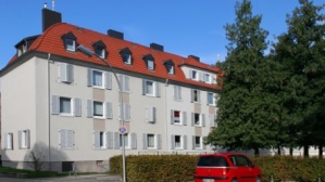 Teil einer sanierten Gebäudezeile, Altbau, 4 Etagen, Klappläden. Rechts zwei hohe Bäume, Parkplatz.