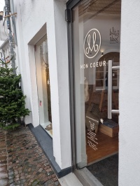 Pop-up-Store Mon Coeur Schräger Blick auf die Eingangstür des Mon Coeur-Pop-up-Stores mit Schriftzug und Logo des Betriebs, am Rand link steht ein Tannenbaum