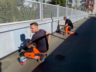 Männer in Warnkleidung streichen eine Mauer und ein Geländer