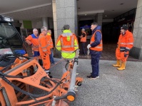 Menschen in Warnwesten stehen mit einem Reinigungsfahrzeug in einer Einkaufsstraße