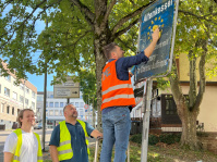 Menschen mit Warnwesten und Müllsäcken reinigen ein Schild