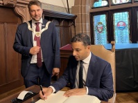 Der Botschafter der Vereinigten Arabischen Emirate, S.E. Ahmed Alattar, hat sich bei seinem Besuch im Rathaus am 1. September, in das Goldene Buch der Stadt ein. Ein Mann sitzt schreibend auf einem Stuhl, ein anderer steht neben ihm