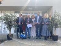 Mehrere Erwachsene stehen vor einem Gebäude an einem Band und Zerschneiden es als Symbol einer Eröffnung