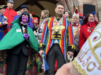 Mehrere kostümierte Personen stehen vor dem Rathauseingang, während ein Mann im bunten Kostüm neben einer Person mit grünem Umhang posiert.