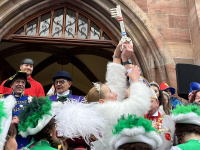 Eine Frau im weißen Fellumhang hebt vor dem Rathausportal einen großen symbolischen Schlüssel in die Höhe, während kostümierte Personen um sie herum stehen.