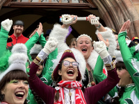 ine Gruppe kostümierter Personen steht dicht gedrängt auf den Treppen des Rathauses, während im Hintergrund Seifenblasen in die Luft steigen.
