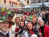 Eine Gruppe bunt geschminkter und kostümierter Personen posiert für ein Selfie vor einer dichten Zuschauermenge.