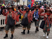 Vier Frauen in karierten Jacken, Hüten und Stiefeln marschieren beim Umzug durch die Straße und winken lachend ins Publikum.