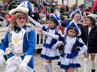 Ein Mann in blau-weißem Uniformkostüm läuft voran, hinter ihm tanzen mehrere Mädchen in passenden blau-weißen Gardekostümen.