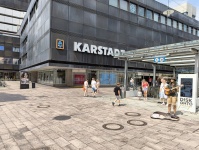 Eine belebte Fußgängerzone mit einem Straßenmusiker im Vordergrund und Kaufhaus im Hintergrund 
