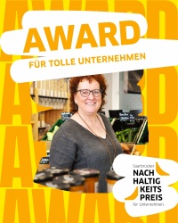 „Eine lächelnde Person steht in einem Unverpackt-Laden vor Regalen mit Lebensmitteln und Obst- und Gemüsekisten. Darüber steht der Schriftzug ‚AWARD FÜR TOLLE UNTERNEHMEN‘ auf gelb-orangem Hintergrund. Unten rechts ist das Logo des ‚Saarbrücker Nachhaltig